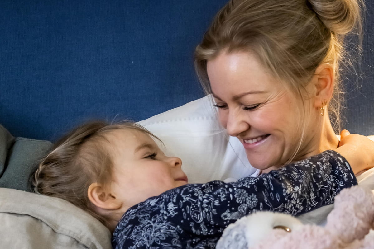 Kvinna och flicka kramas och myser bland kuddar