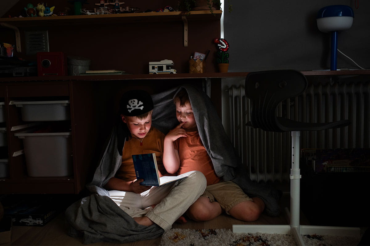 Barn läser med en ficklampa under en filt.