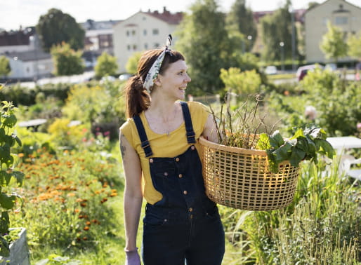 Kvinna i trädgård håller i en korg med grönsaker