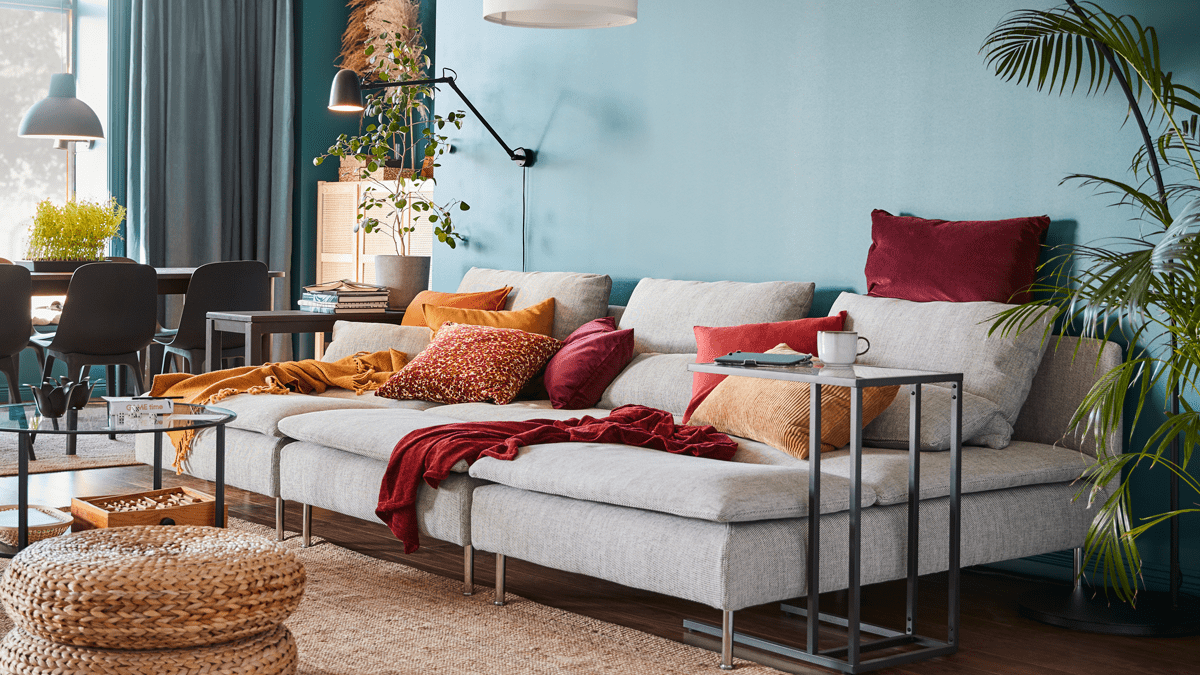 Ett öppet vardagsrum med grå soffa och kuddar i orange och vinröda toner.