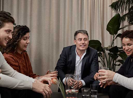 Människor på ett kontor sitter runt ett bord och dricker vatten.