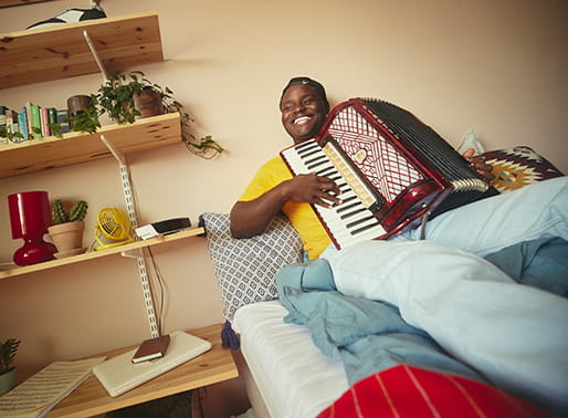 Glad ung man sitter i soffan och spelar dragspel.