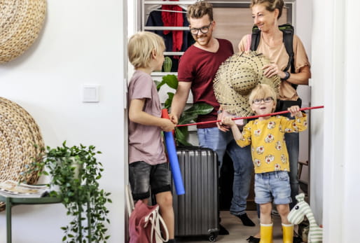Mamma, pappa och två barn står i hallen med resväskor.