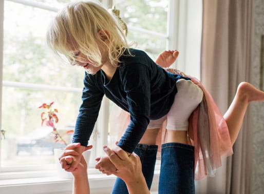 Glad flicka ligger som ett flygplan över ett par vuxenfötter.