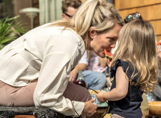 Kvinna böjer sig fram och blir matad med vattenmelon av en liten flicka.