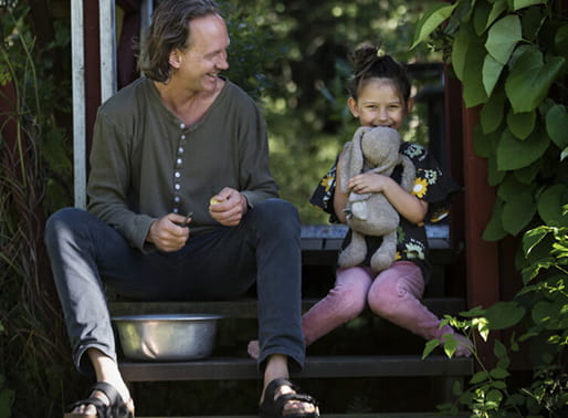 Barn med gosedjur sitter med pappa och skalar potatis