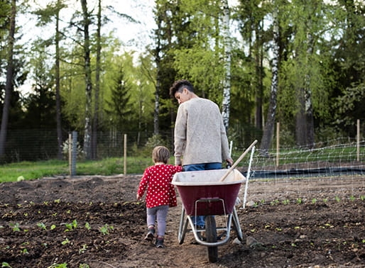 Kvinna och barn drar skottkärra bakom sig i trädgårdsland.