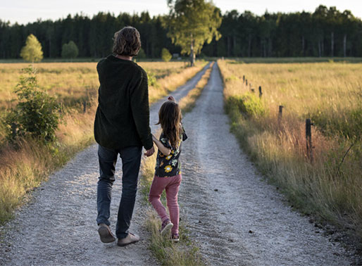 Förälder och barn går längs grusväg i solnedgång.