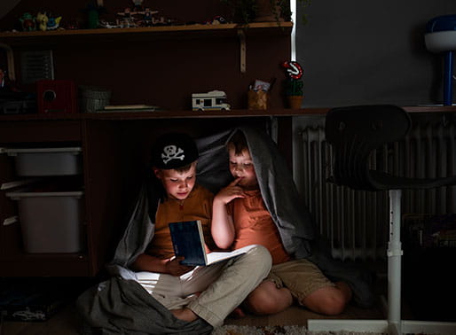 Barn i tält läser bok med ficklampa.