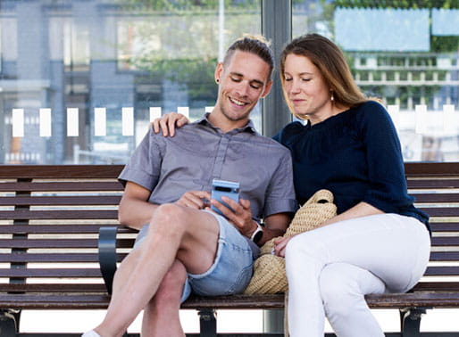 Par sitter på tågstation och tittar på mobil.