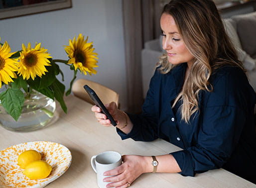 Kvinna scrollar på mobilen vid köksbordet.