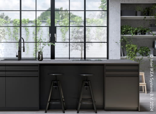 En svart köksö i ett grått kök med stora fina fönster.